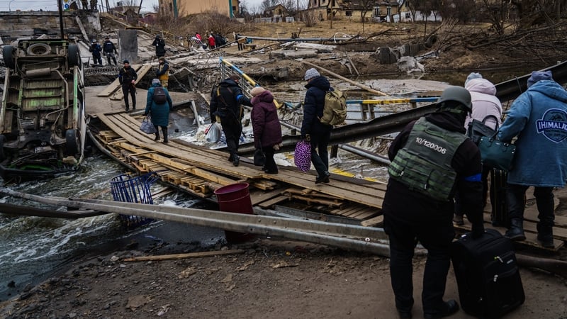 Ukrainian soldiers help civilians cross a makeshift walkway over a destroyed bridge to evacuate out of Irpin