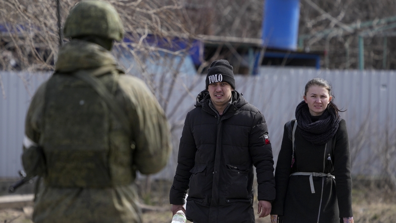 Lánúin as Mariupol ag tarraingt go faiteach ar phointe seiceála; ní léir cén t-arm gur de é an saighdiúir