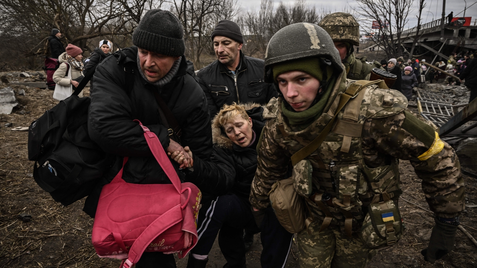 A woman is assisted while people cross a destroyed bridge as they evacuate the city of Irpin