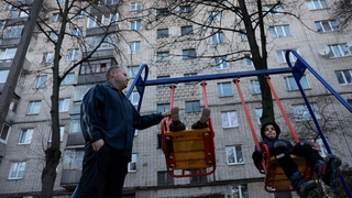 A man plays with his children on a swing outside their apartment complex in Lviv today