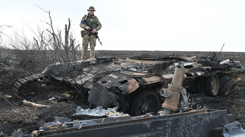 A Ukrainian soldier stands on the wreckage of a burnt Russian tank outside Mala Rogan, east of Kharkiv, Ukraine