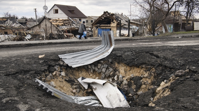 A local resident walks past a bomb crater in Demydiv