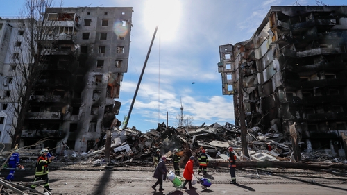 People walk by a severely damaged residential building in Bucha