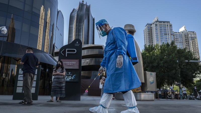 A health worker sprays disinfectant as people wait on a Covid-19 test at a testing site in Beijing