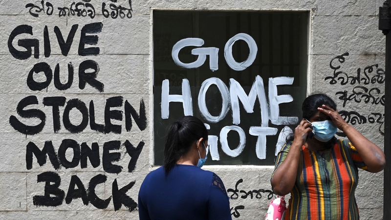 Women stand in front of a graffiti painted outside the premises of Sri Lanka's presidential palace, in Colombo