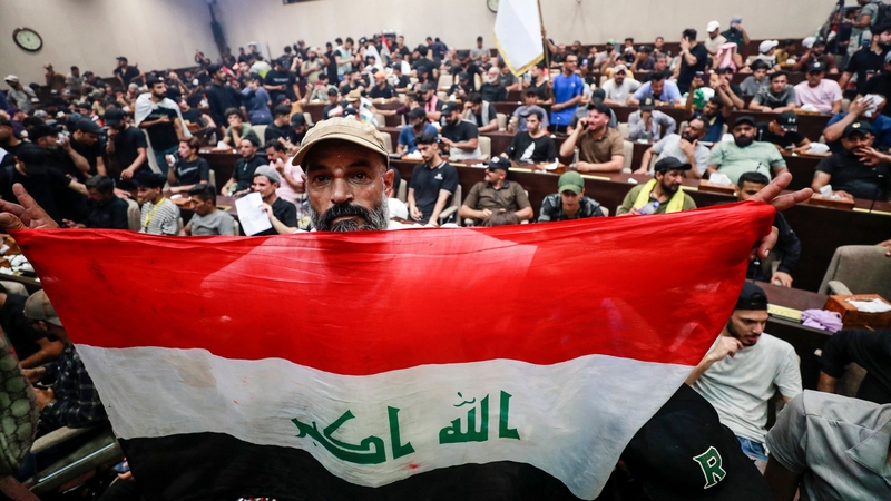 A man deploys a national flag as supporters of the Iraqi cleric Moqtada Sadr gather inside the country's parliament in the capital Baghdad's high-security Green Zone
