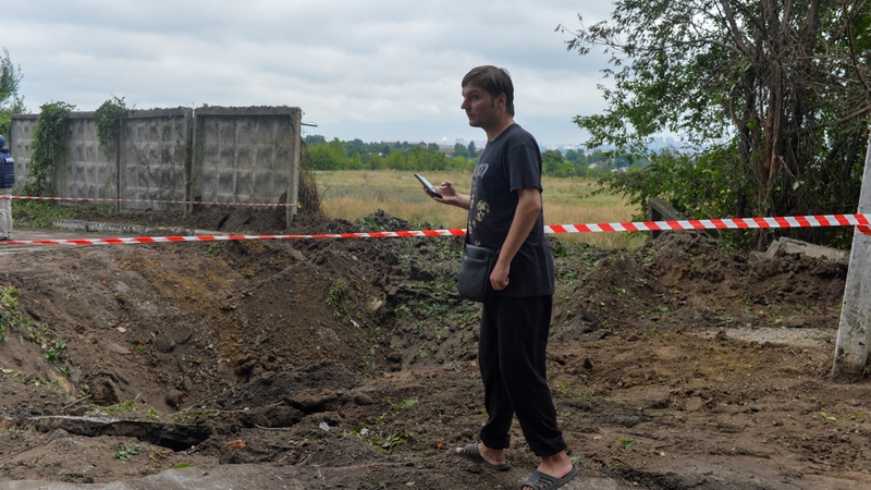 A Ukrainian man takes a photo of an explosion crater formed after the night-long bombardment of Russian troops in Kharkiv