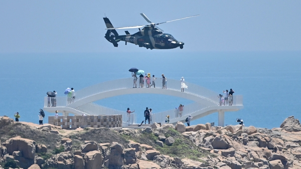 Tourists look on as a Chinese military helicopter flies past Pingtan island, China, ahead of massive military drills off Taiwan