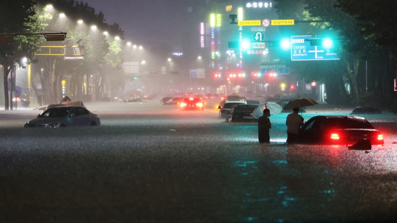 Men stand among vehicles abandoned in flooded area during heavy rain in Seoul