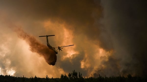A firefighting aircraft sprays fire retardant over trees during a wildfire near Belin-Beliet in Gironde