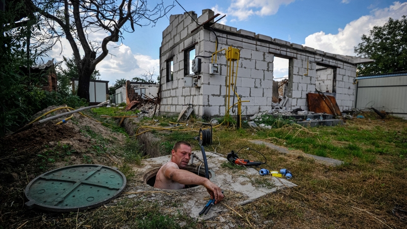 A man repairs a water pipe near his destroyed house in the village of Andriivka, Kyiv region