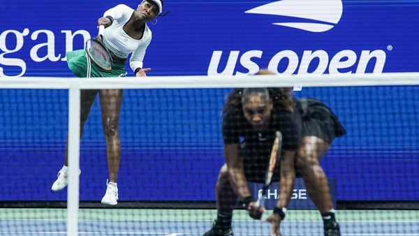 Venus Williams serves with Serena Williams at the net in what is expected to be their last Grand Slam doubles appearance