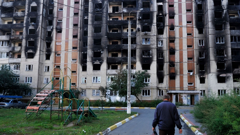 A man walks towards a damaged residential building in the town of Irpin