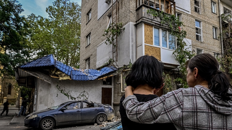 Two women stand in front of a damaged building in Mykolaiv