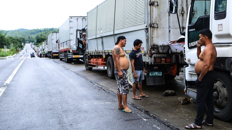 Drivers stand next to cargo trucks lined up on a highway in southern Philippines after ferry service was halted due to Tropical Storm Nalgae