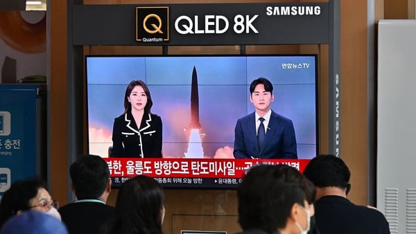 People watch a TV screen showing a news broadcast with file footage of a North Korean missile test
