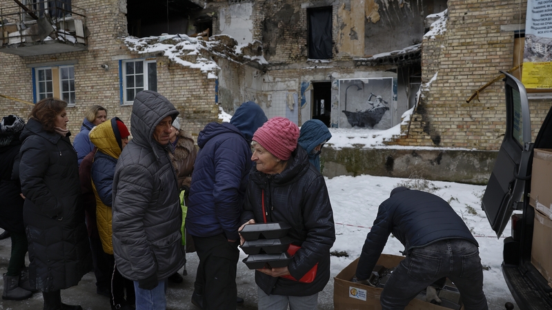 Members of the public queue for food beside a picture by graffiti artist Banksy in Horenka, Ukraine