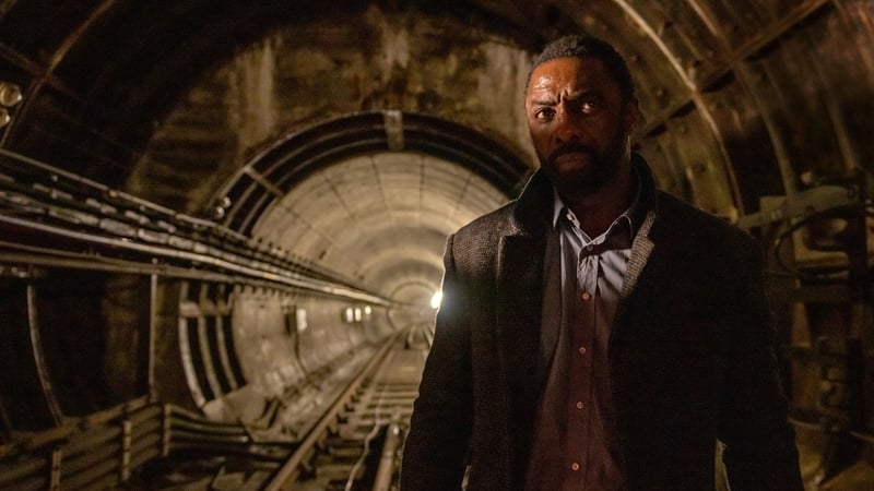 Idris Elba can be seen in an underground tunnel, sporting an inquisitive expression