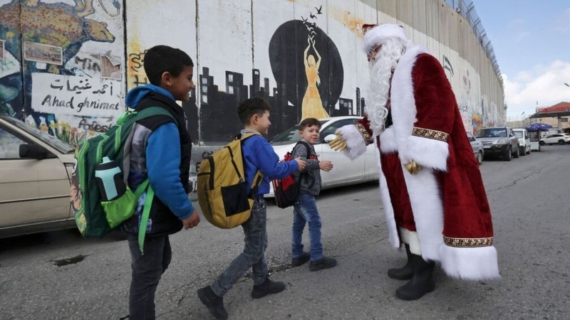 Santa greets children on a street alongside Israel's separation wall in the biblical West Bank city Bethlehem, ahead of Christmas