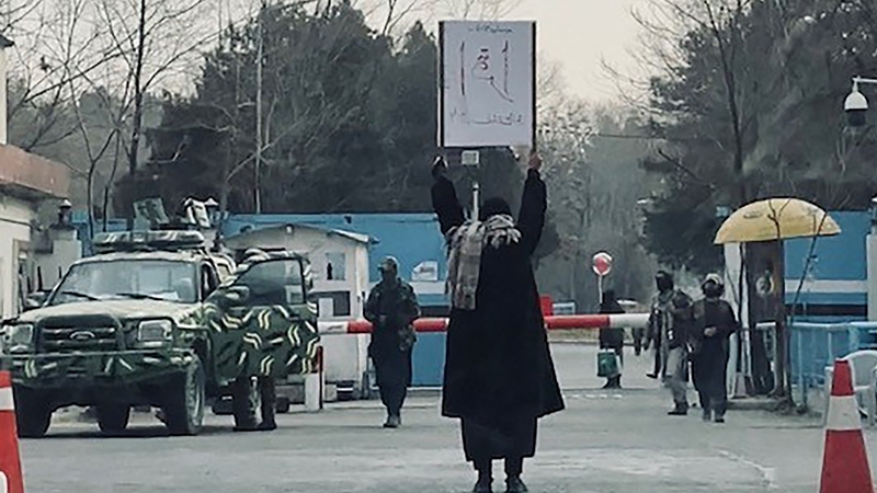 A student protesting alone outside the Kabul University as members of Taliban stand guard