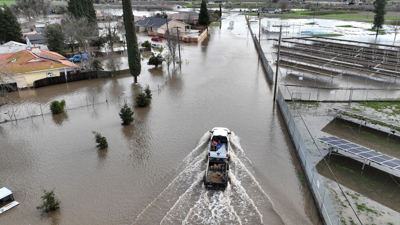 A vehicle drives on a flooded roadway in Planada, California