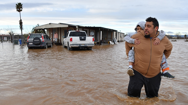 Ryan Orosco carries his son Johnny, 7, while his wife Amanda waits to be rescued from their flooded home in Brentwood
