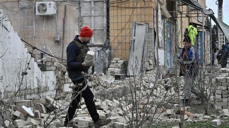 People clear debris next to a shop damaged following a strike in Kherson today