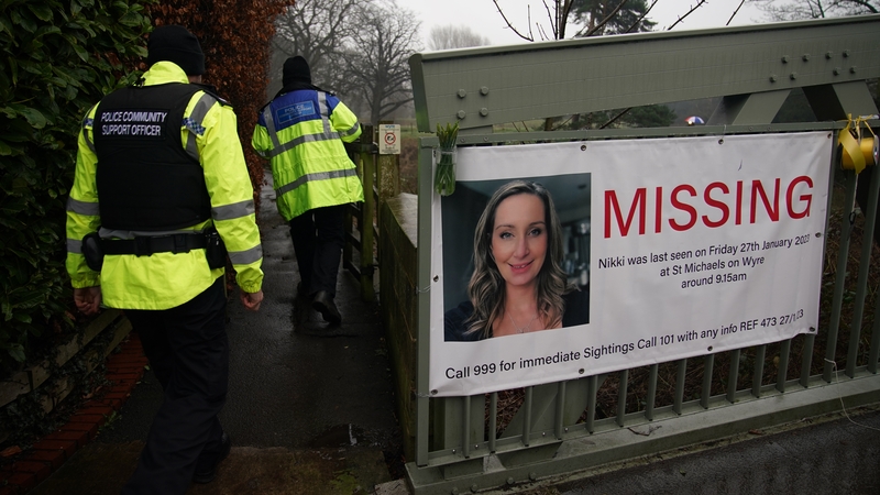 Police officers walk past a missing person appeal poster for Nicola Bulley tied to a bridge over the River Wyre