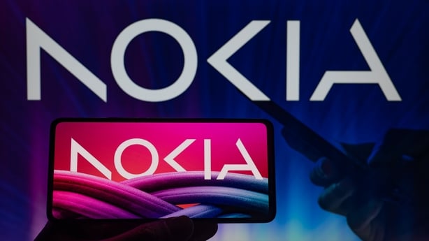 a hand holding a phone with the new Nokia logo on it against a background with Nokia written on it
