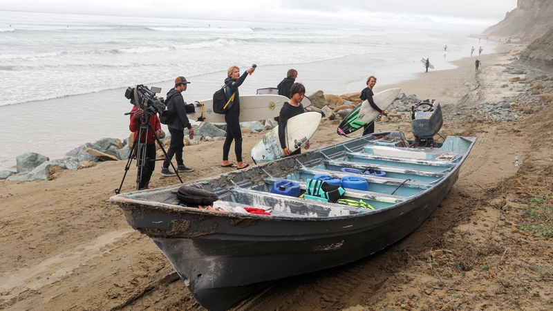 Surfers walk by a 'panga' boat sitting along the Black's Beach, after two panga fishing boats capsized off the coast of San Diego