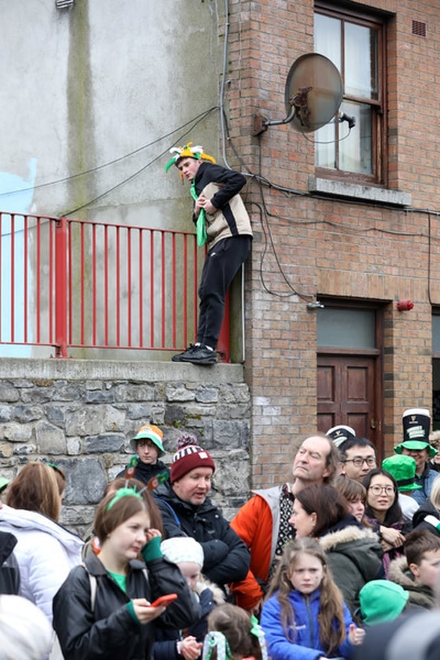 Trying to get a better view. A young man climbs a fence in Dublin to see the parade (Image: Rolling News)