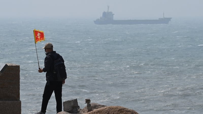 A man walks with a flag as a ship passes by behind him on Pingtan island, the closest point to Taiwan, in China's southeast Fujian province