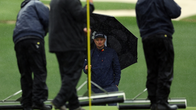 Staff try to clear the greens of water as Justin Rose looks on