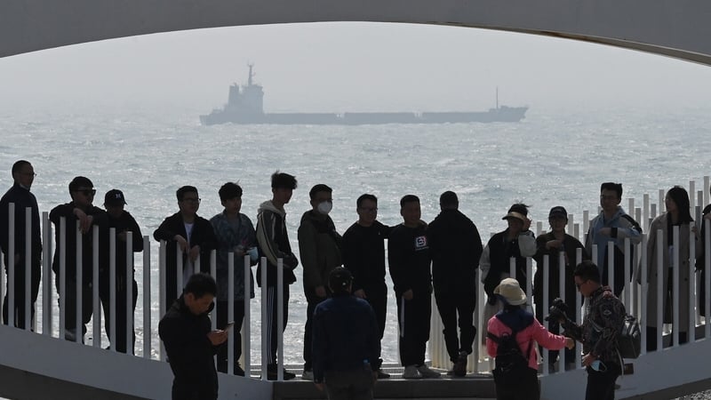 A ship sails in the Taiwan Strait, past tourists standing on a viewing platform on Pingtan island