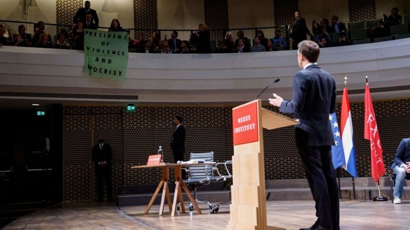 Protesters display a banner during Emmanuel Macron's speech in The Hague