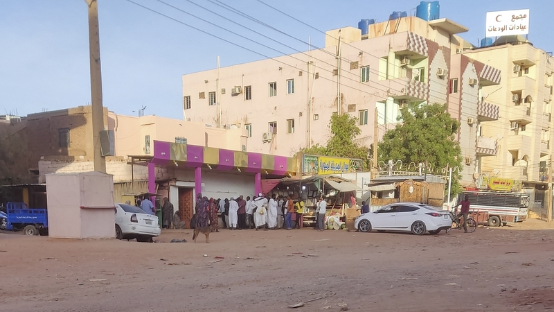 People rush to buy fresh produce from a shop on an almost empty street in southern Khartoum
