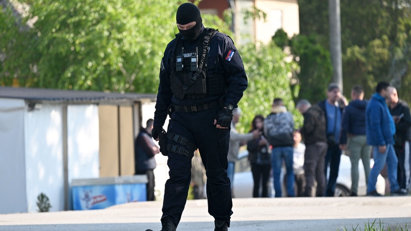 A masked policeman secures an area in the village of Dubona near the town of Mladenovac in the aftermath of a drive-by shooting