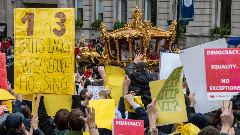 Protesters hold signs and shout as King Charles and Queen Camilla pass by after the coronation ceremony