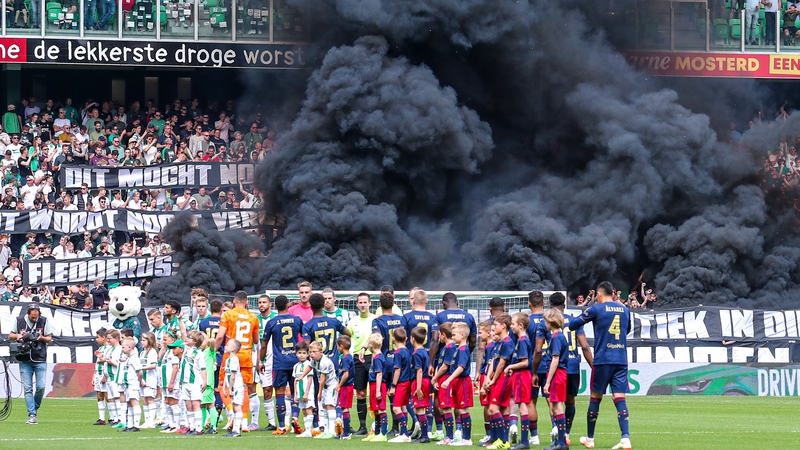 Players from both teams on the pitch with smoke in the background
