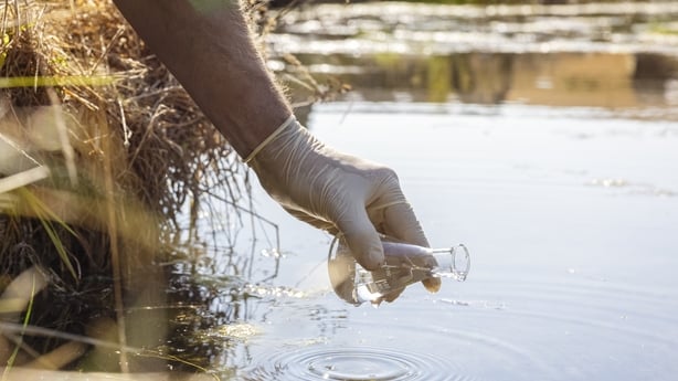 A gloved hand puts a scientific jar into water.