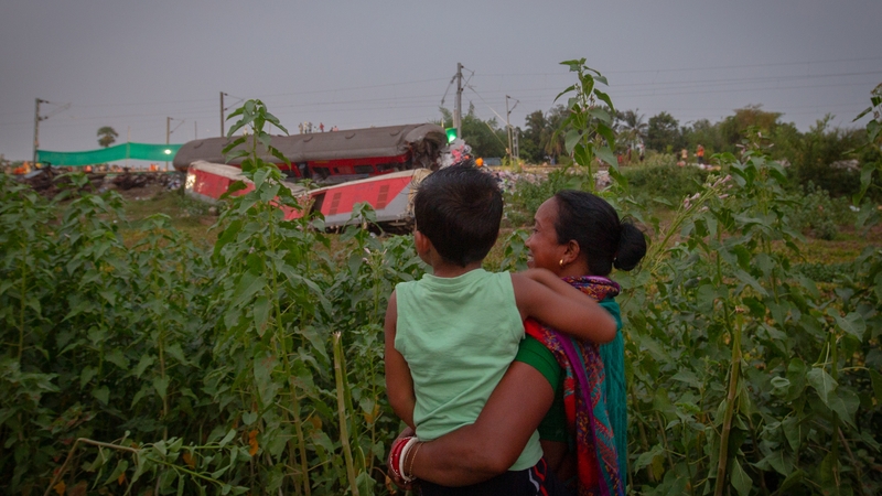 A woman holds a child and looks at the wreckage of a rail coach on Saturday