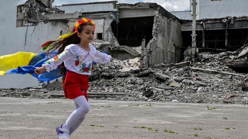 A child runs as she holds a Ukrainian flag in front of the destroyed building of a cultural centre, hit in a missile strike, during a graduation ceremony in the town of Derhachi