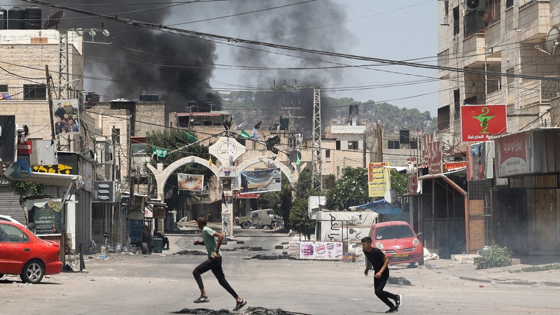 Palestinian youths run for cover amid clashes during an Israeli military operation in Jenin city in the occupied West Bank