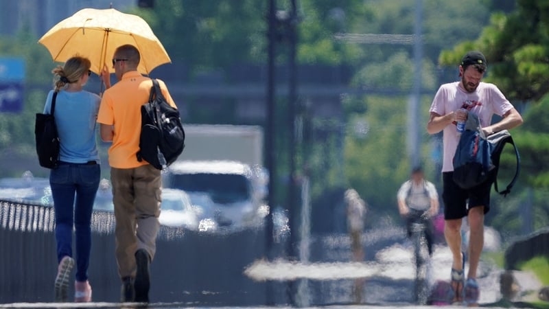 People walk by the Imperial Palace Gardens in the intense heat in Tokyo