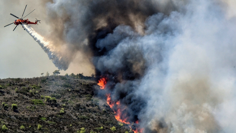 A Sikorsky firefighting helicopter drops water on a wildfire near Agioi Theodori, some 70km west of Athens on 18 July