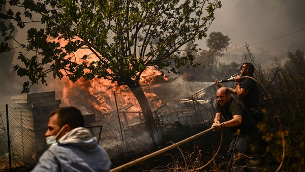 Men spray water on a wildfire in Chasia on the outskirts of Athens