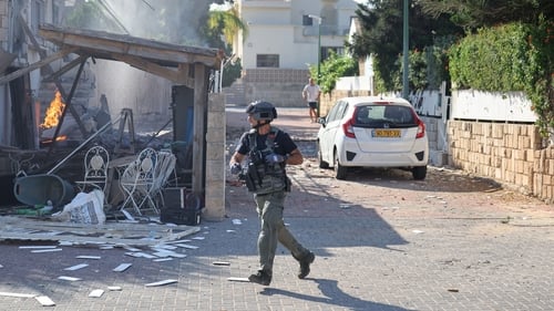 An Israeli soldier runs by a house damaged in a rocket attack in Ashkelon