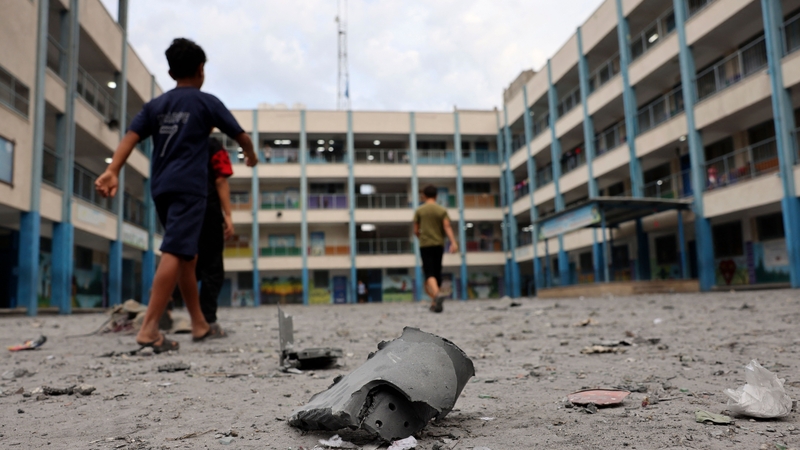Palestinian children walk past debris at a school run by the United Nations Relief and Works Agency for Palestine refugees (UNRWA) today