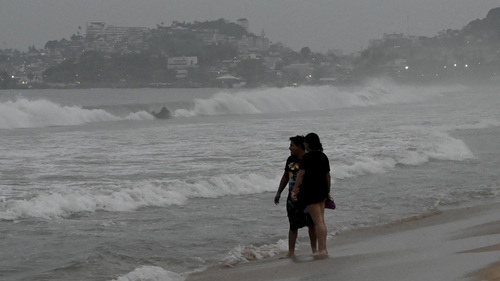 People watch waves on a beach in Acapulco ahead of the expected arrival of Hurricane Otis