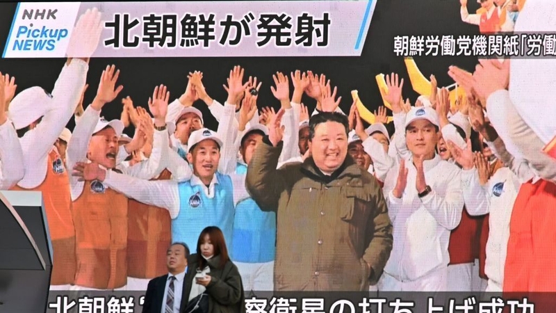 Pedestrians walk past a screen displaying Kim Jong-un celebrating after the reconnaissance satellite 'Malligyong-1' was launched